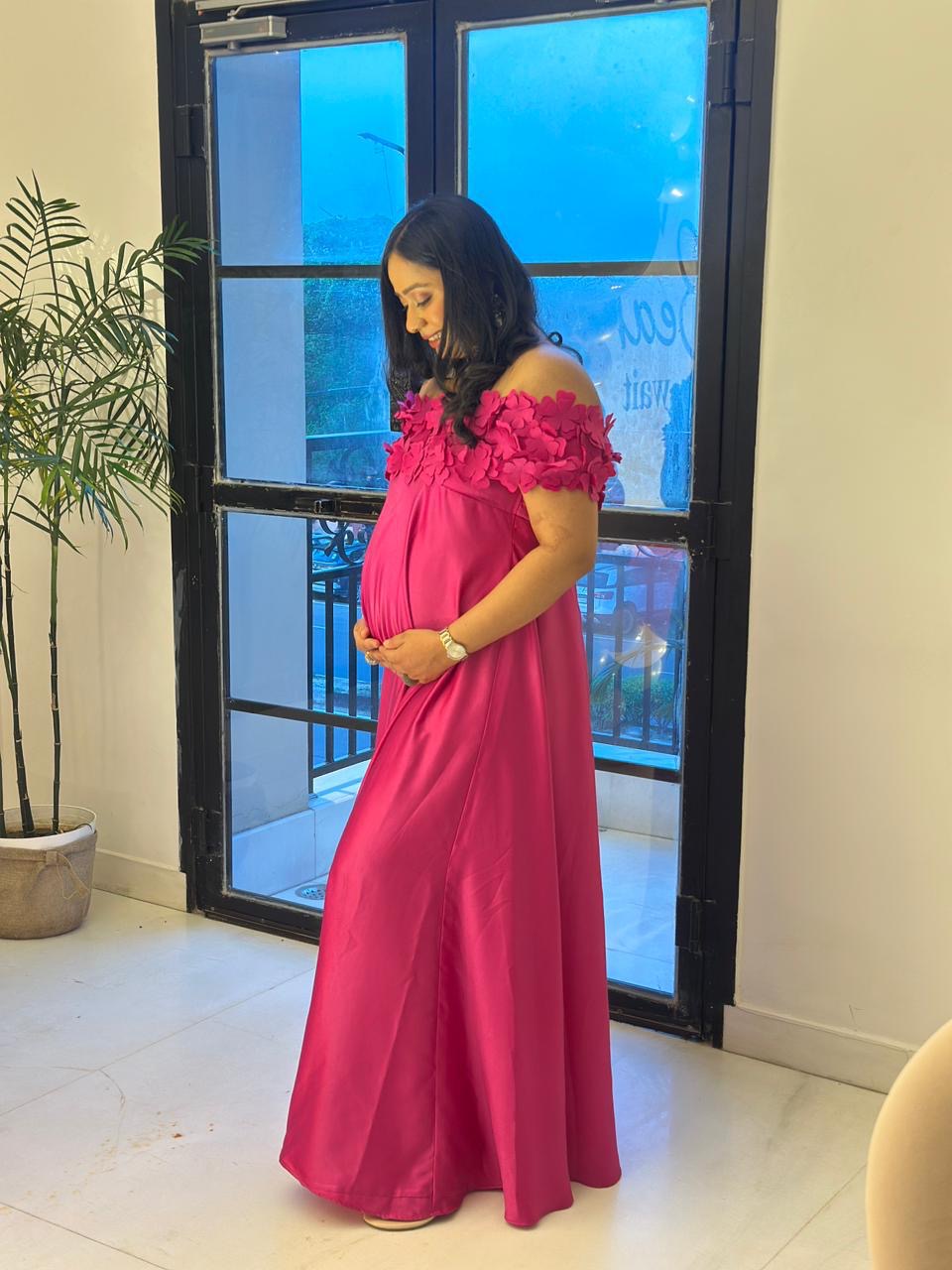 Woman in a pink dress standing indoors near a glass door.